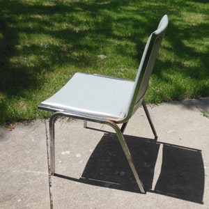 May include: A silver metal chair with a white padded seat. The chair is on a gray concrete surface.