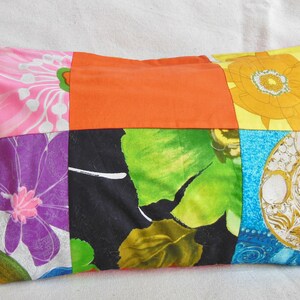 May include: A rectangular patchwork pillow featuring a variety of floral and geometric patterns. The pillow's design incorporates squares of pink, orange, yellow, green, and blue fabrics. The pillow is filled and has a soft appearance.