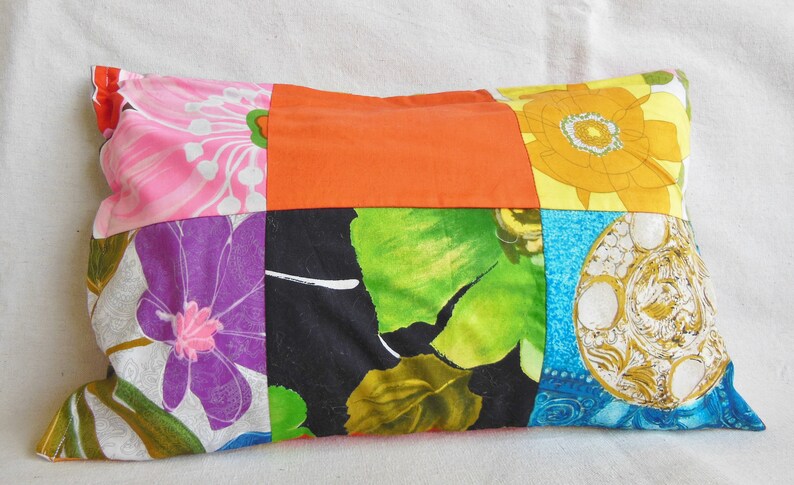 May include: A rectangular patchwork pillow featuring a variety of floral and geometric patterns. The pillow's design incorporates squares of pink, orange, yellow, green, and blue fabrics. The pillow is filled and has a soft appearance.