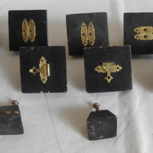 May include: Ten black wooden cabinet knobs with gold metal hinges. The knobs are square and have a simple design.