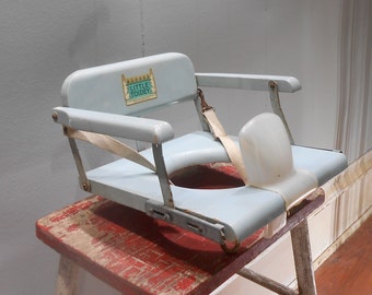 May include: A light blue vintage Little Tondey potty chair with a white strap and a white plastic back support. The chair is sitting on a red wooden stool.