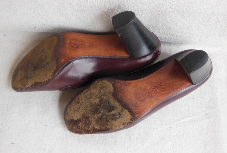 May include: A pair of burgundy leather shoes with a low heel. The shoes have a worn leather sole.