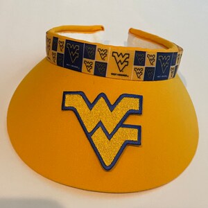 May include: A yellow visor with a blue and gold West Virginia University logo embroidered on the front. The visor has a blue and gold ribbon with the West Virginia University logo repeated on it.