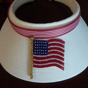 May include: White visor with a red and white striped band and a beaded American flag pin.