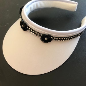 May include: White visor with a black rhinestone trim and black flower embellishments.
