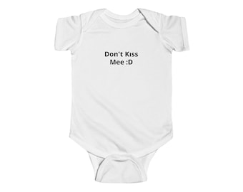 Puede incluir: Un body blanco de manga corta para bebé con el texto impreso en negro Don't Kiss Mee :D centrado en el pecho. La prenda cuenta con un cuello redondo, mangas cortas y un cierre de botones a presión en la parte inferior para facilitar el cambio.