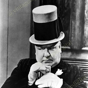 May include: Black and white image of a man wearing a top hat and a pinstripe suit. He is holding a playing card and wearing white gloves. The hat has a light-colored brim and a dark crown.