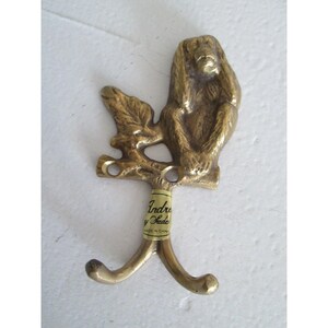 May include: A brass wall hook featuring a monkey perched on a branch. The hook has two curved prongs and a small tag that reads "Indre y Sade". The monkey is in a seated position with its hands covering its ears.