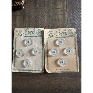 May include: Two vintage button cards with clear, flower-shaped buttons. Each card has four buttons on a tan background. The cards are labeled "Nu Style" in script with a green border. The buttons have a silver center.