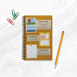 Könnte beinhalten: Ein spiralgebundenes Notizbuch mit senffarbenem Einband, das Notizen zu Gestaltungsprinzipien enthält. Das Notizbuch hat einen gelben Bleistift und bunte Büroklammern. Text enthält "Drittel-Regel", "Goldener Schnitt" und "Optisches Zentrum".