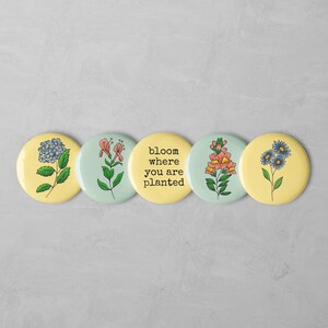 May include: Five yellow and blue round buttons with floral designs and the text "bloom where you are planted".