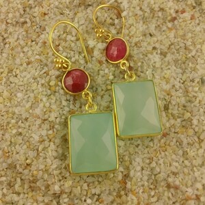 May include: A pair of gold earrings with a light green rectangular gemstone and a small red round gemstone on each earring.