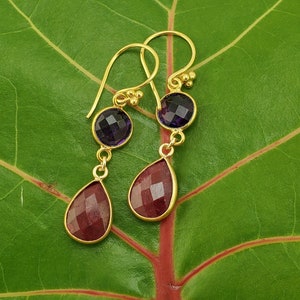 May include: A pair of gold earrings with a teardrop-shaped red gemstone and a round purple gemstone.
