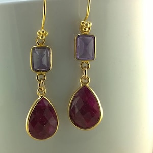 May include: A pair of gold dangle earrings with a purple rectangular stone and a teardrop-shaped red stone on each earring.