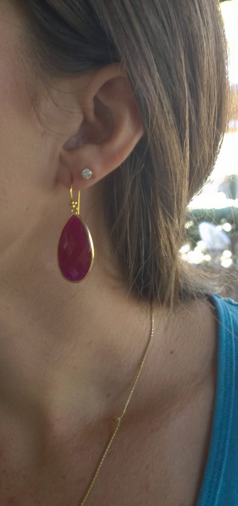 May include: A pair of gold earrings with a teardrop-shaped red gemstone. The earrings are dangling from the earlobe.
