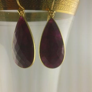 May include: A pair of gold dangle earrings with a teardrop-shaped purple gemstone.