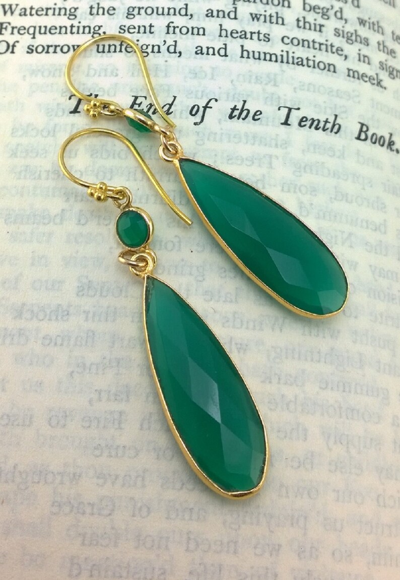 May include: A pair of gold earrings with green gemstone drops. The earrings have a teardrop shape and are accented with smaller round green gemstones.