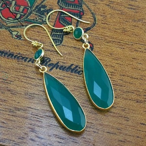 May include: A pair of gold-toned dangle earrings with green gemstone drops. The earrings feature a smaller round green gemstone at the top of each drop.