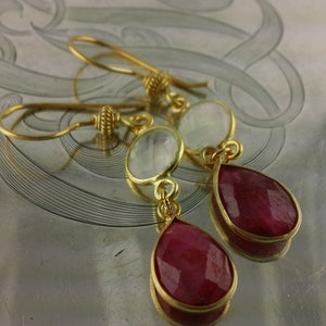 May include: Gold earrings with a teardrop-shaped red gemstone and a round white gemstone.
