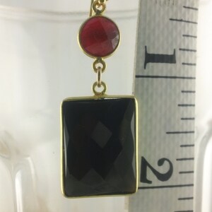 May include: Gold dangle earrings with a black rectangular gemstone and a smaller round red gemstone.