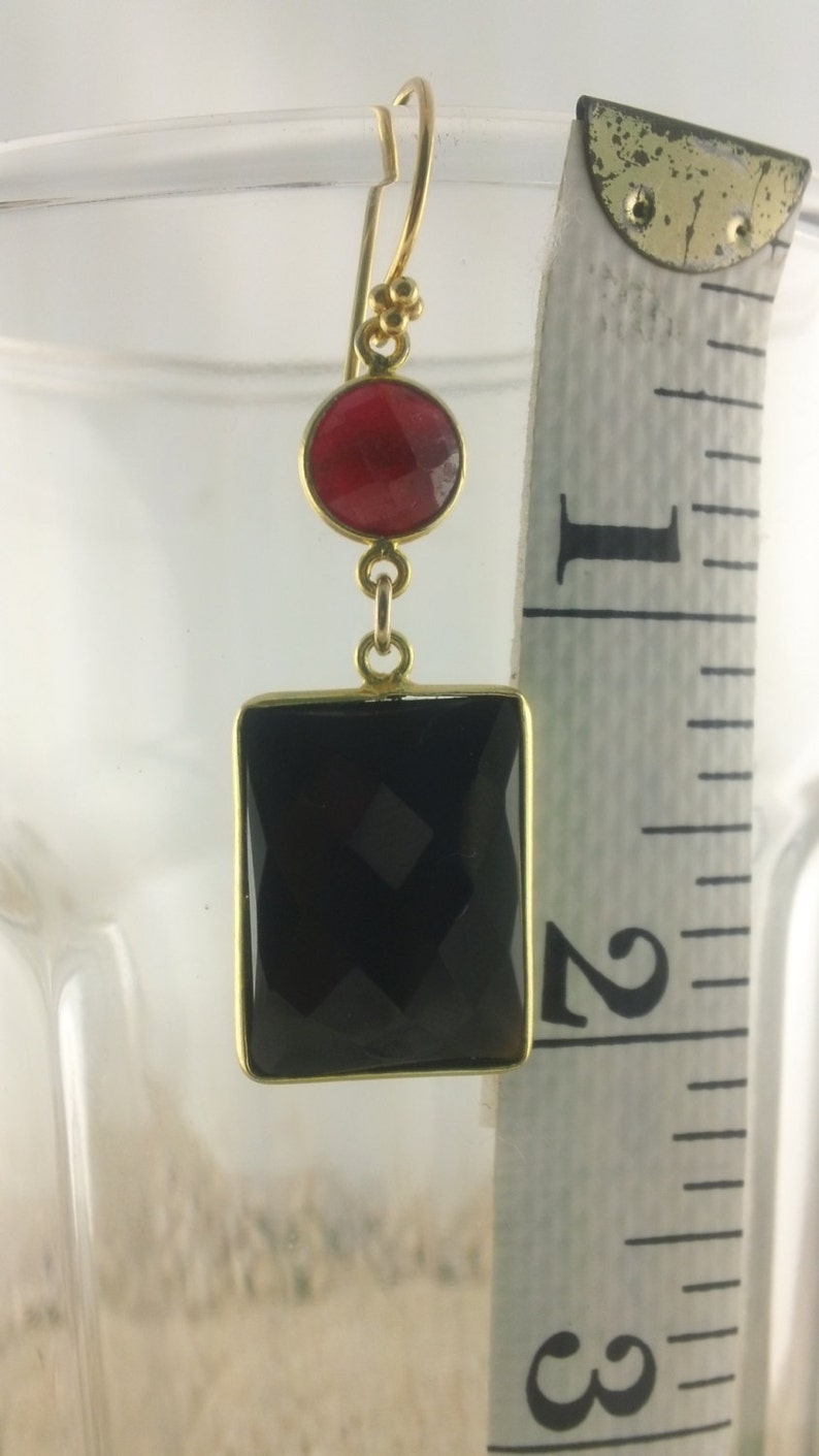 May include: Gold dangle earrings with a black rectangular gemstone and a smaller round red gemstone.
