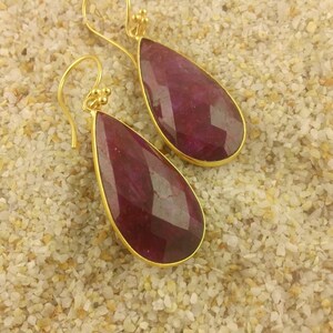 May include: A pair of gold dangle earrings with teardrop-shaped ruby red stones.
