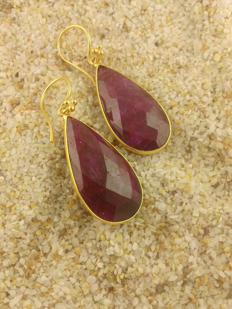 May include: A pair of gold dangle earrings with teardrop-shaped ruby red stones.