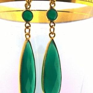 May include: A pair of gold dangle earrings with green gemstone drops. The earrings have a teardrop shape and are accented with smaller green gemstones.