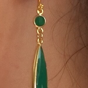 May include: Gold dangle earrings with a green teardrop-shaped gemstone and a smaller round green gemstone.