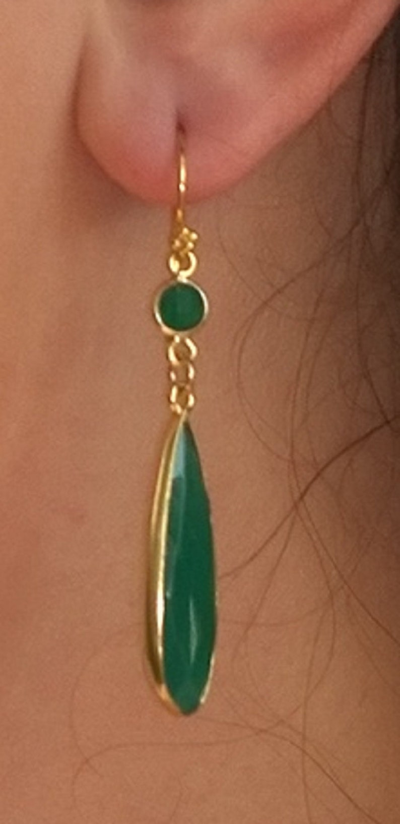 May include: Gold dangle earrings with a green teardrop-shaped gemstone and a smaller round green gemstone.