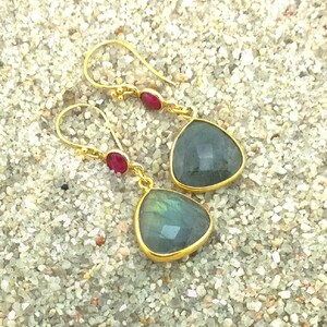 May include: A pair of gold earrings with a teardrop-shaped labradorite gemstone and a small red gemstone accent.