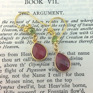 May include: A pair of gold earrings with red gemstone drops and green gemstone accents. The earrings are hanging from a book with the text "Paradise Lost. Book VII. The Argument."