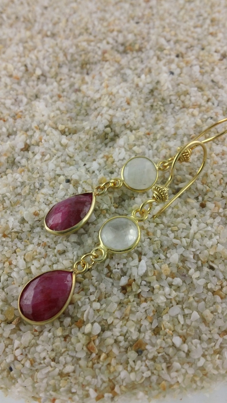 Op de afbeelding: Gouden oorhangers met twee traanvormige rode edelstenen en twee ronde witte edelstenen.
