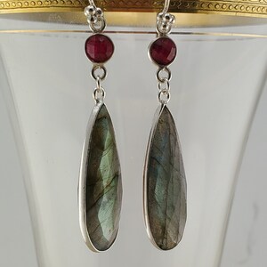 May include: Silver dangle earrings with a teardrop-shaped green labradorite gemstone and a small red ruby accent.