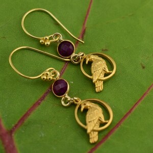 May include: Gold earrings with a purple gemstone and a detailed raven design.