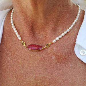 May include: A white pearl necklace with a red and green gemstone pendant.