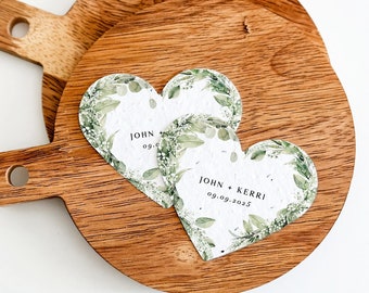 May include: Two wooden round serving trays with a heart-shaped paper card on top. The card is decorated with green leaves and the text "JOHN + KERRI 09.09.2023".