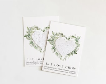May include: Two rectangular white cards featuring a textured, heart-shaped piece of seed paper centered within a printed green watercolor wreath. The text reads LET LOVE GROW, followed by planting instructions in black, sans-serif font.