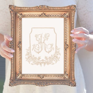 May include: A gold framed print with a white background and a gold monogram of the letters "J" and "K" surrounded by a floral design.
