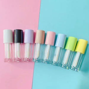 May include: A row of eight clear lip gloss tubes with applicator wands inside. The caps are colored white, black, lavender, beige, light pink, light blue, lime green, and yellow, arranged in a line against a split pink and blue background.