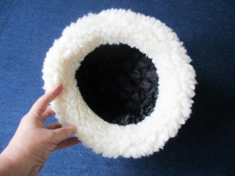 Puede incluir: Sombrero de piel sint&eacute;tica blanca con forro negro. El sombrero es redondo y tiene un ala ancha.