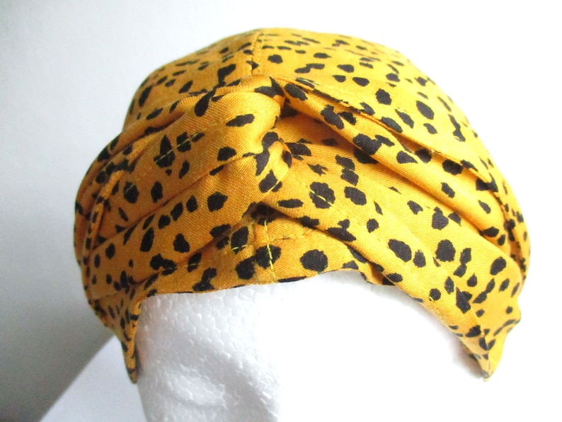 Pode incluir: Um turbante amarelo com um padr&atilde;o de leopardo preto. O turbante &eacute; feito de tecido e &eacute; dobrado para criar um n&oacute; no topo.