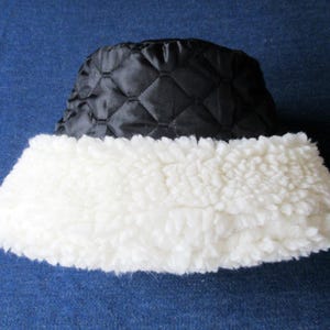 Puede incluir: Un gorro de cubo acolchado negro con un borde de piel sint&eacute;tica blanca. El gorro est&aacute; hecho de un material suave y c&aacute;lido, perfecto para el clima fr&iacute;o.