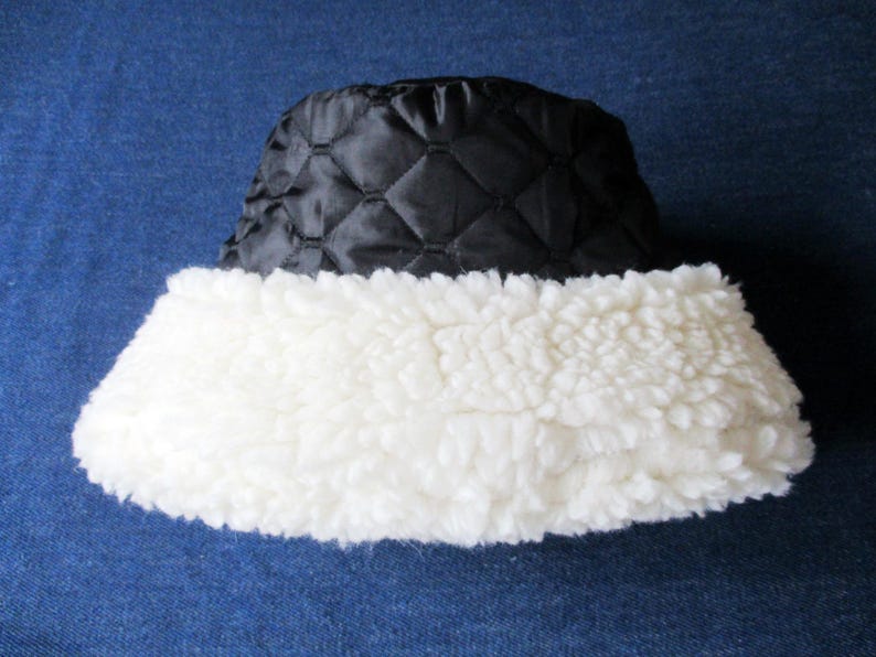Puede incluir: Un gorro de cubo acolchado negro con un borde de piel sint&eacute;tica blanca. El gorro est&aacute; hecho de un material suave y c&aacute;lido, perfecto para el clima fr&iacute;o.