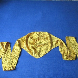 Pode incluir: Uma echarpe amarela com padr&atilde;o de leopardo preto. A echarpe est&aacute; amarrada em um n&oacute; no topo e as pontas est&atilde;o penduradas.