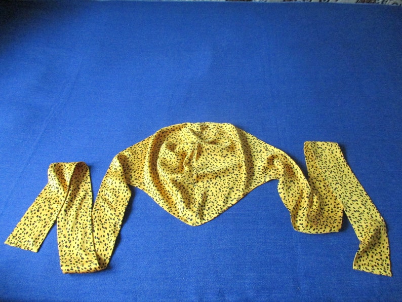 Pode incluir: Uma echarpe amarela com padr&atilde;o de leopardo preto. A echarpe est&aacute; amarrada em um n&oacute; no topo e as pontas est&atilde;o penduradas.