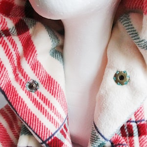 May include: Close-up of a red and white plaid hooded jacket with a white fleece lining. The jacket has two metal poppers on the collar.