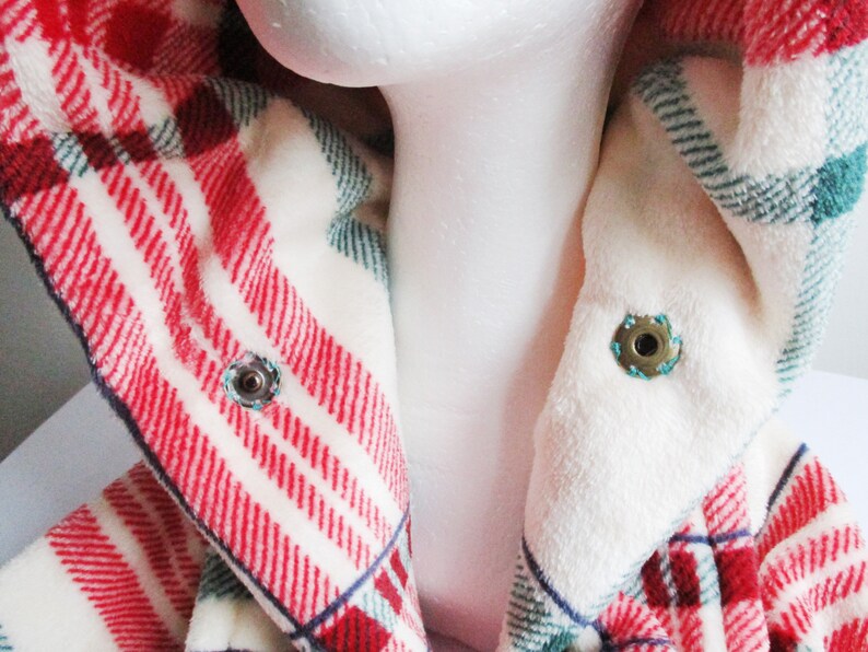 May include: Close-up of a red and white plaid hooded jacket with a white fleece lining. The jacket has two metal poppers on the collar.