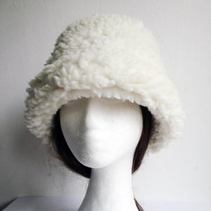 Puede incluir: Un gorro blanco y esponjoso de estilo bucket hecho de piel sint&eacute;tica. El gorro es suave y tiene un ala ancha.