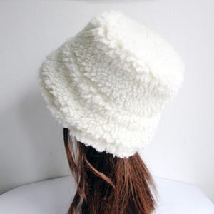 Puede incluir: Un gorro de cubo blanco y esponjoso hecho de tela suave y texturizada.